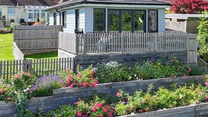 Une véranda dotée d’une terrasse en bois, entourée d’un jardin où poussent différentes variétés de fleurs.