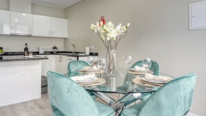A modern kitchen with white cabinets, a central island, and a dining area with a glass table and teal chairs. - Tristão Vaz I, a Home in Madeira (Machico)