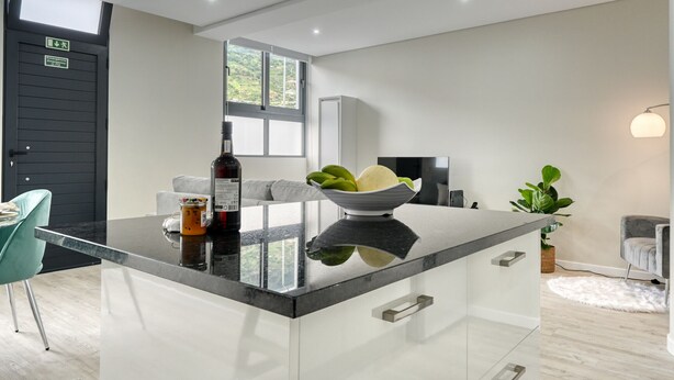A modern kitchen with a central island, a black door, a window, and a plant. - Tristão Vaz I, a Home in Madeira (Machico)