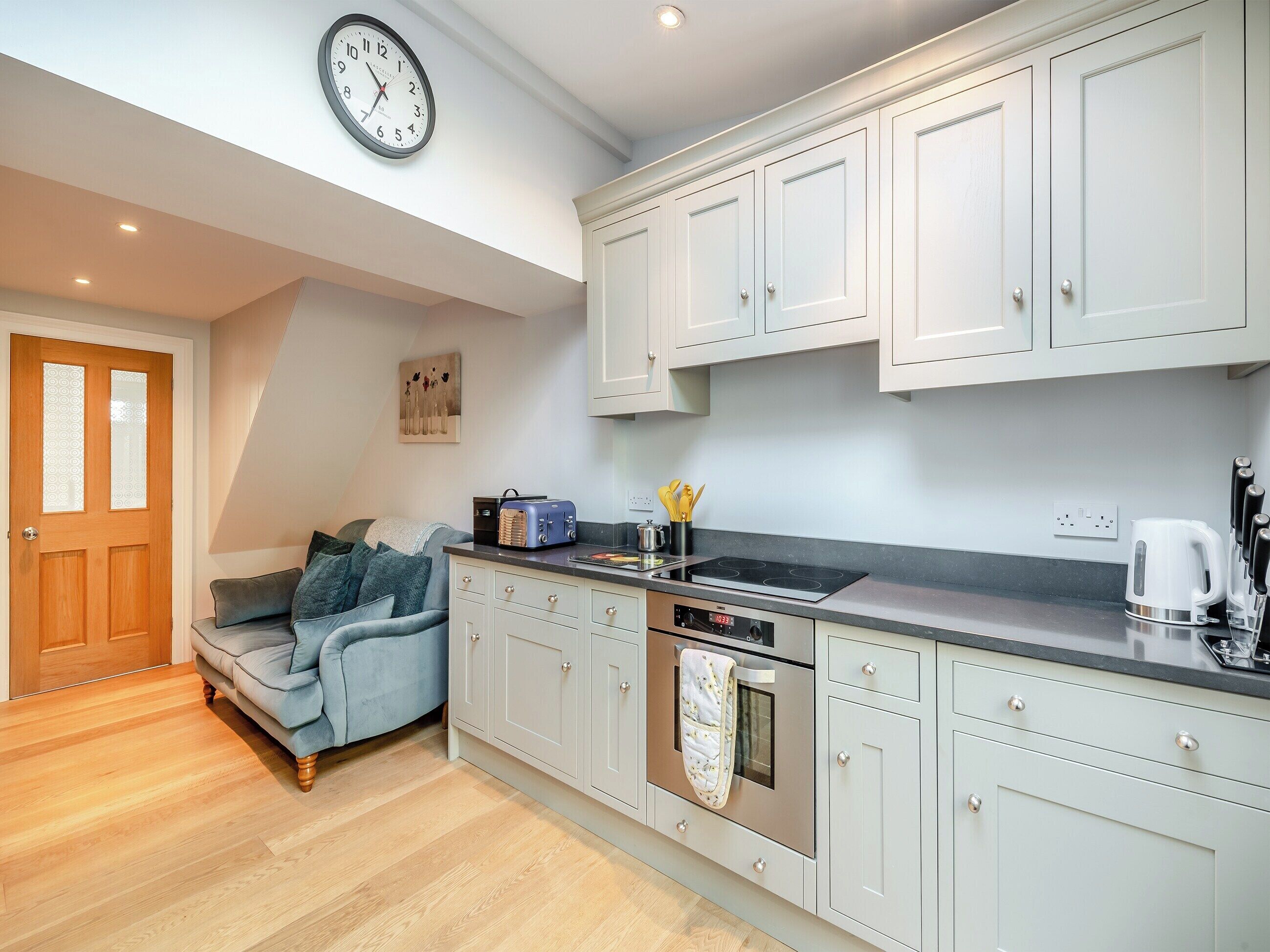 A modern kitchen with white cabinets, a built-in oven, and a clock on the wall.