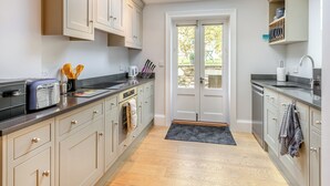Une cuisine moderne avec des meubles de couleur claire, un plan de travail noir, une lucarne et une vue sur l’extérieur grâce à une porte vitrée.