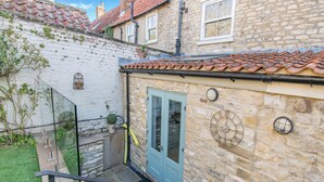 Un bâtiment en pierre avec une porte bleue, une horloge et un petit jardin agrémenté de plantes en pot.