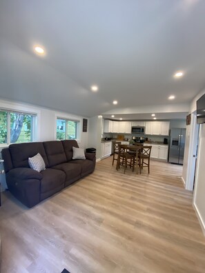 A modern living room with a brown sofa and a dining area with wooden chairs.