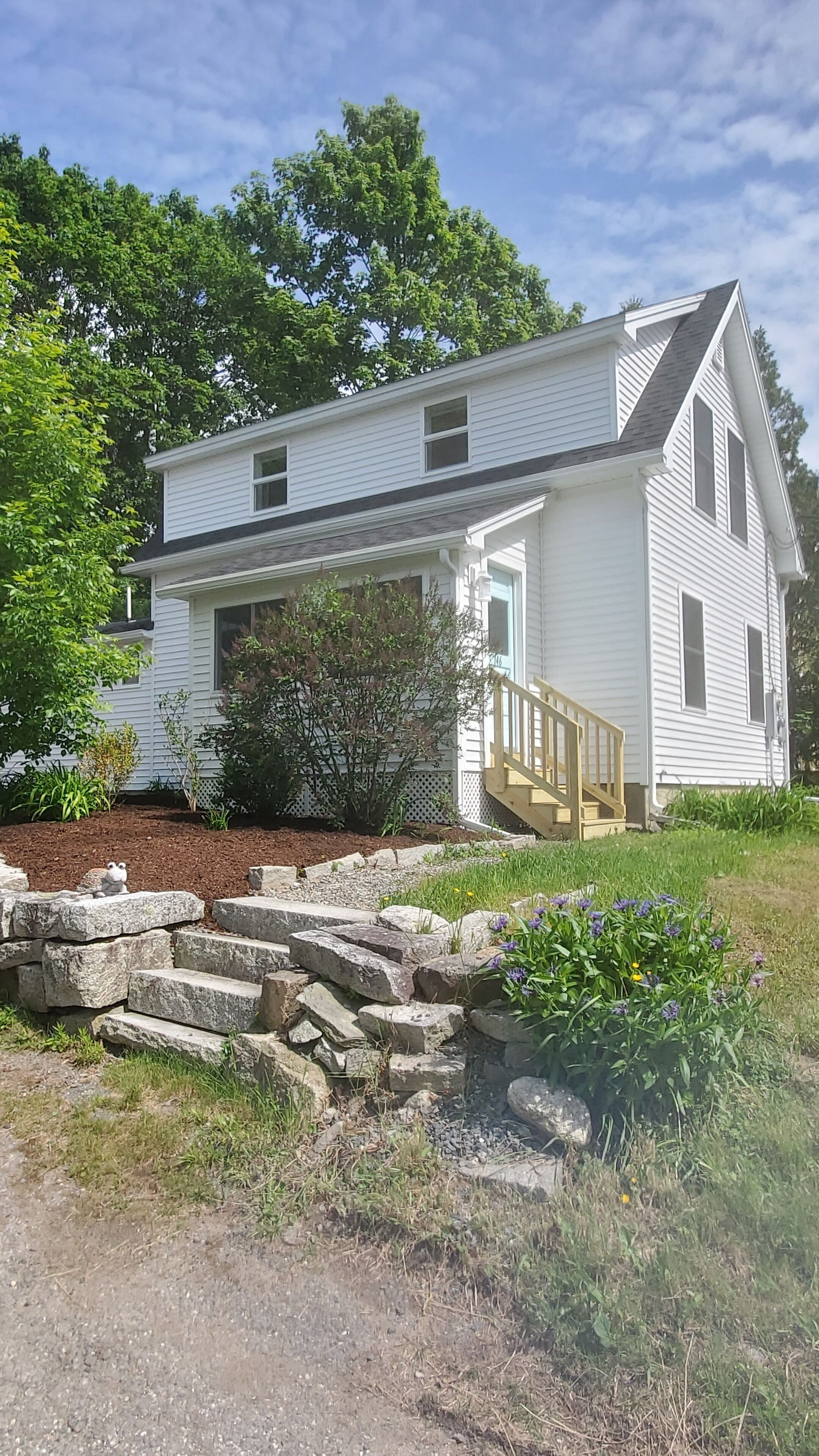 A two-story white house with a covered porch and a stone retaining wall.