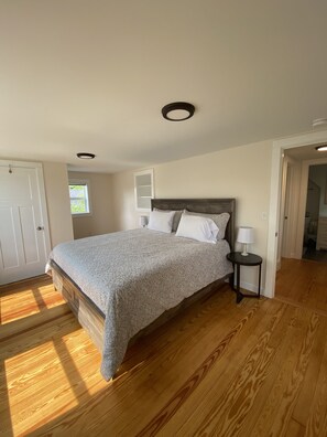 A bedroom with a bed, a nightstand, a window, and a door.