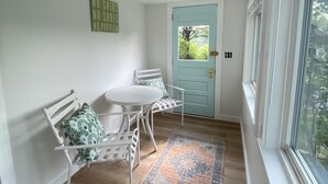 Une pièce avec un banc blanc, une petite table blanche, un tapis à motifs et une porte bleu clair.