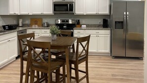Une cuisine moderne avec des meubles blancs, des appareils en acier inoxydable et une table à manger en bois, accompagnée de chaises.