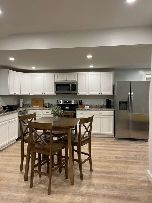 A modern kitchen with white cabinets, stainless steel appliances, and a wooden dining table with chairs.