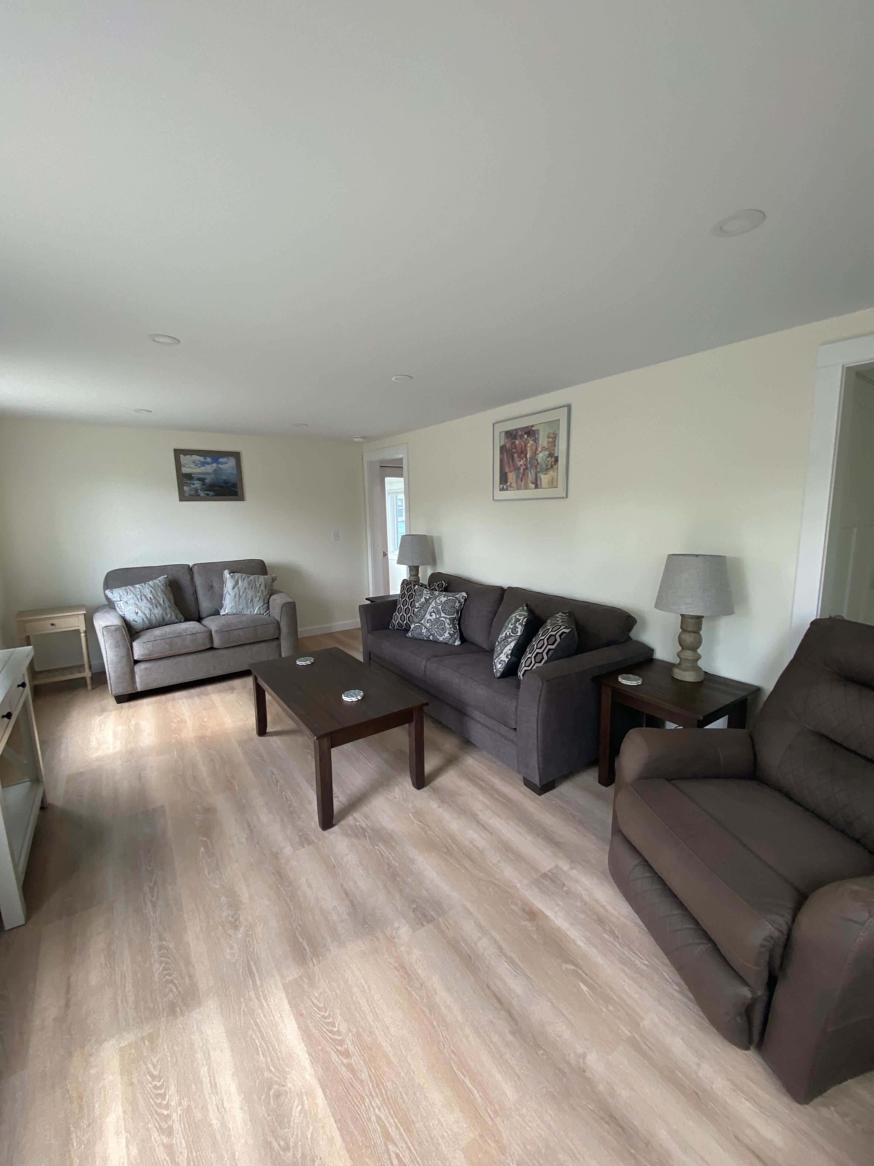 A living room with a grey sofa, a brown sofa, and a brown armchair. There are two wooden coffee tables and two lamps.