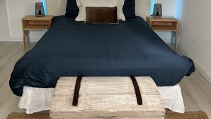 A bedroom with a bed, two bedside tables, a nightstand, a wooden chest, and a blue ceiling light.