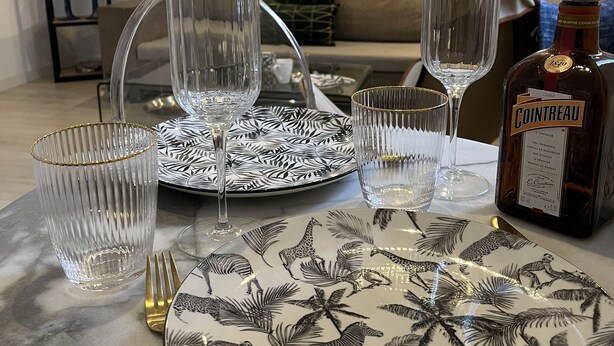 A dining table set with plates, glasses, and cutlery, a bottle of Cointreau, and a bookshelf in the background.