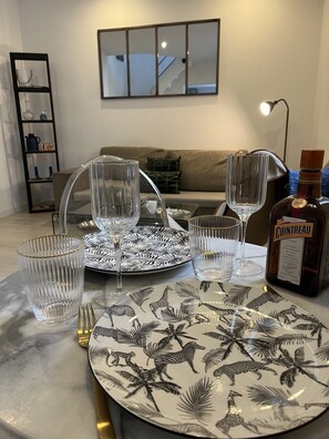 Une table à manger dressée avec des assiettes, des verres et des couverts, une bouteille de Cointreau, et une bibliothèque en arrière-plan.