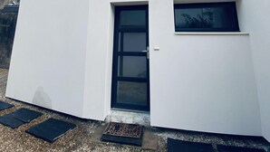 A modern white building with a black door, a small window, and a metal railing on the roof.