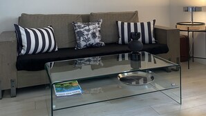 A modern living room with a glass coffee table, a sofa with striped and floral cushions, and a large mirror on the wall.