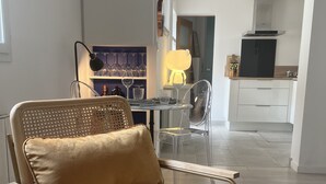 A modern living room with a leather armchair, a dining table with chairs, a kitchen area, and a large window.