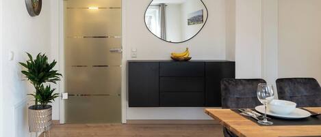 Un comedor moderno con una mesa de madera, sillas negras, un armario negro y un espejo en la pared.