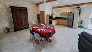Un coin repas avec un mur en pierre, des poutres en bois, un grand buffet et une cuisine en arrière-plan.