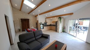 Un vaste espace de vie avec un canapé foncé, une table basse en bois et une cuisine en arrière-plan.