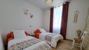 Une chambre avec deux lits, une petite table, une chaise et une fenêtre avec des rideaux.
