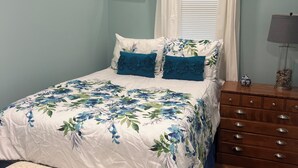 Een slaapkamer met een bed, een dressoir, een bankje en een raam met gordijnen.