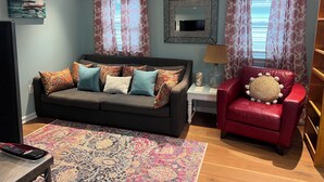 Een woonkamer met een bank, een rode fauteuil, een televisie en een vloerkleed met dessin.