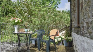 A wooden deck with a table and two chairs, surrounded by greenery and a stone wall. - 1 bedroom accommodation in Lostwithiel (Lostwithiel)