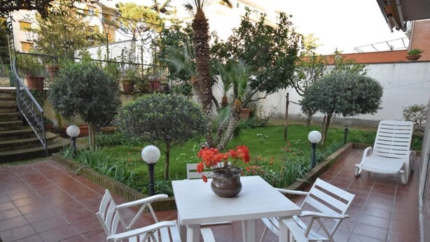 En terrasse med et hvidt bord og stole, omgivet af plantekrukker og en lille have.