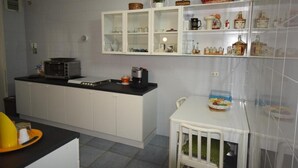 Et kompakt køkken med hvide skabe, en mikroovn, kaffemaskine og et lille spisebord med en stol.