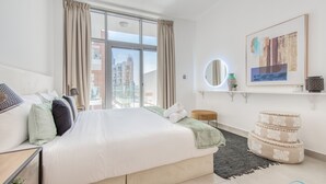 Ett modernt hotellrum med en stor säng, utsikt över staden, en rund spegel och ett inramat konstverk på väggen.