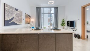 Ett modernt kök med en central köksö, en matplats med två stolar, en tv och konstverk på väggarna.