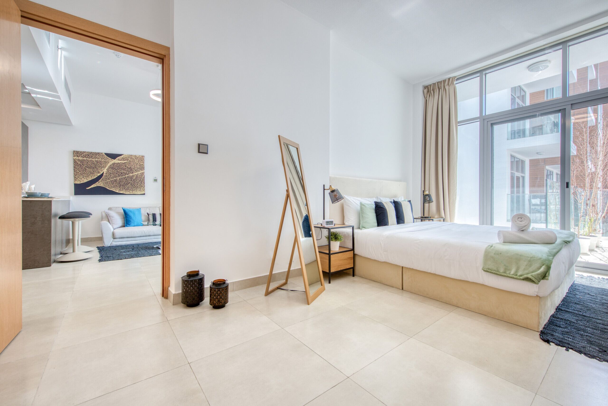 A modern hotel room with a large bed, bedside table, and a view of the city through large windows.