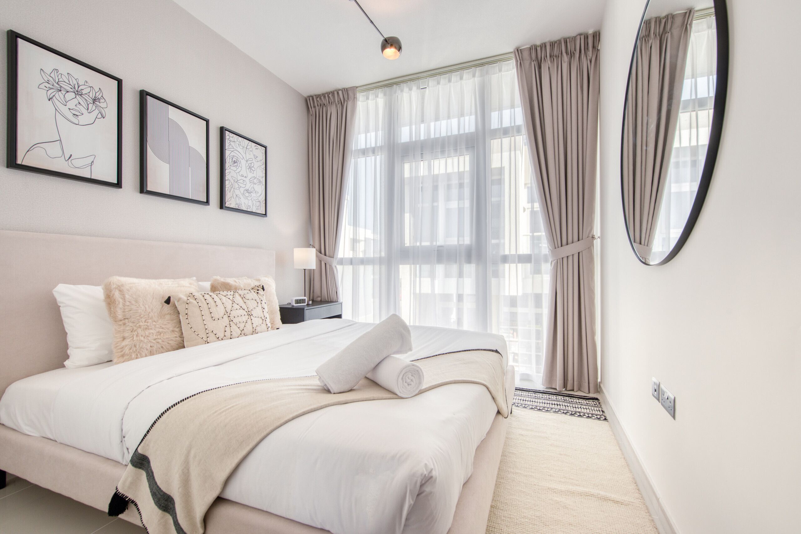 Une chambre à coucher moderne avec un grand lit, une table de chevet avec une lampe et une fenêtre avec des rideaux.