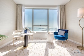 A modern room with a large window, a round table, a blue armchair, and a floor lamp.