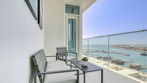 A balcony with a sofa, two chairs, a small table, and a potted plant. The balcony overlooks a marina with boats and a clear view of the water. - Idyllic 1BR at Sunrise Bay Tower 1 Emaar Beachfront Dubai Marina by Deluxe Holiday Homes (Dubai)
