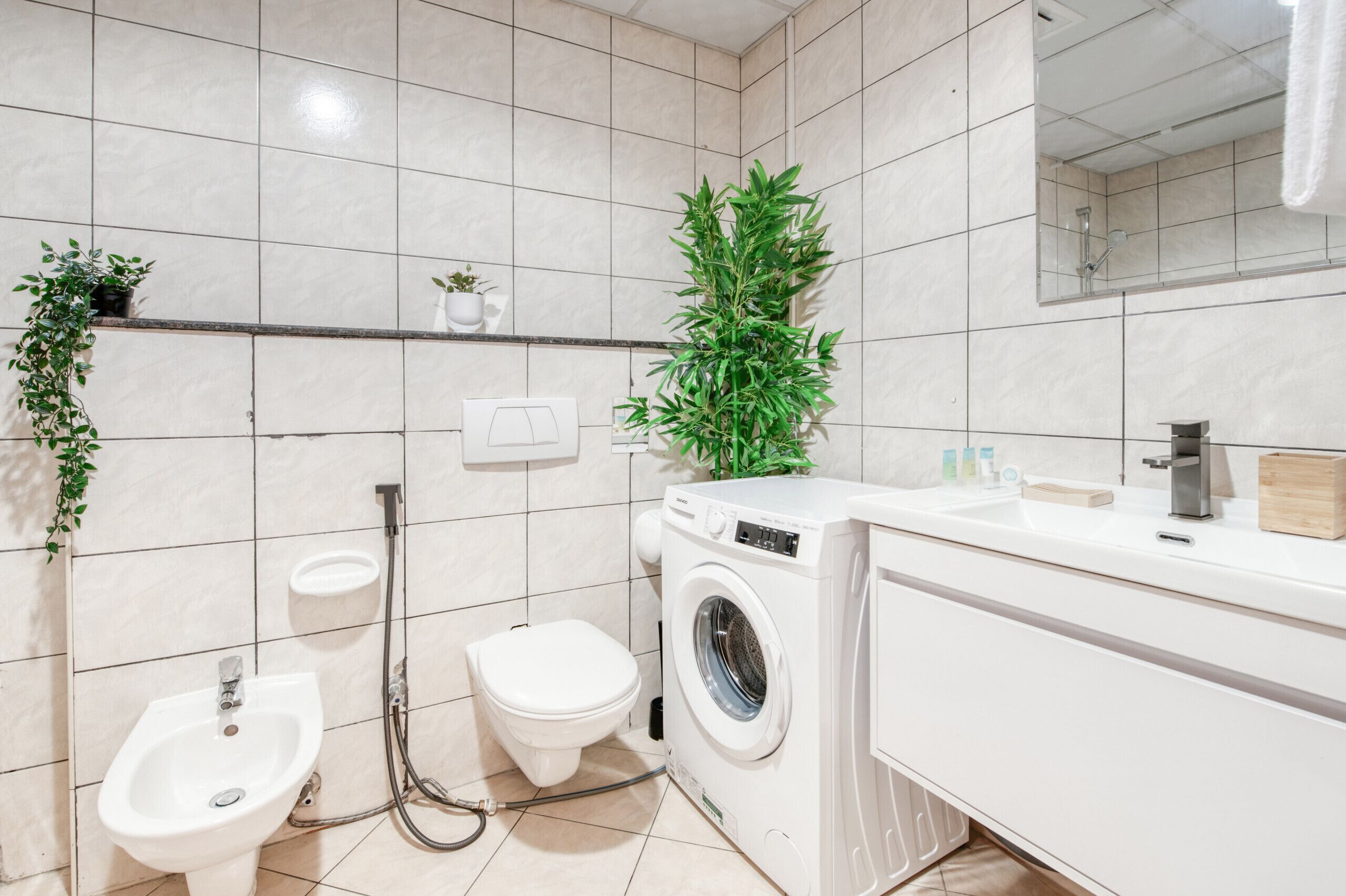 Une salle de bain moderne équipée d’un bidet, de toilettes, d’un lave-linge et d’un lavabo avec un miroir.