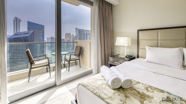Een hotelkamer met een ruim balkon, een bed met witte lakens, een nachtkastje met een lamp en uitzicht op de skyline van de stad.