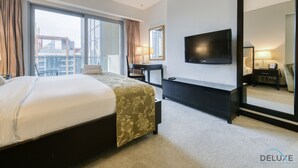 Una habitación de hotel con una cama grande, un escritorio, un televisor y un espejo amplio.