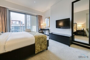 A hotel room with a large bed, a desk, a TV, and a large mirror.