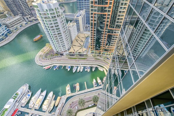 A high-rise building with a marina below, featuring multiple boats docked and a pedestrian walkway.