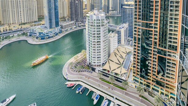 Un edificio alto con fachada curva, un puerto deportivo con barcos y un horizonte urbano al fondo.