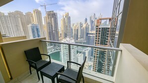 Un balcón con dos sillones de mimbre y vistas a un paisaje urbano con rascacielos y una grúa de construcción.