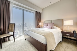 A hotel room with a large bed, two bedside tables, a chair, and a view of the city through large windows.