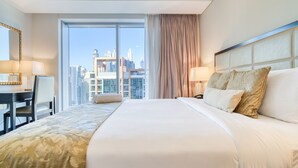 A hotel room with a large bed, a desk, and a chair. There is a view of tall buildings through the window.