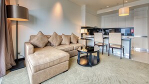 A modern living room with a sofa, a coffee table, and a dining area with chairs and a kitchen in the background.