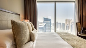 A hotel room with a large bed, a view of the cityscape, and a city skyline visible through the windows.
