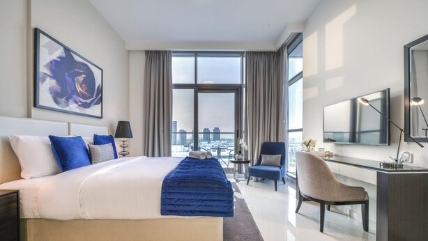 Une chambre d’hôtel moderne, dotée d’un grand lit, d’un bureau, d’une chaise et offrant une vue sur la ville par la fenêtre.