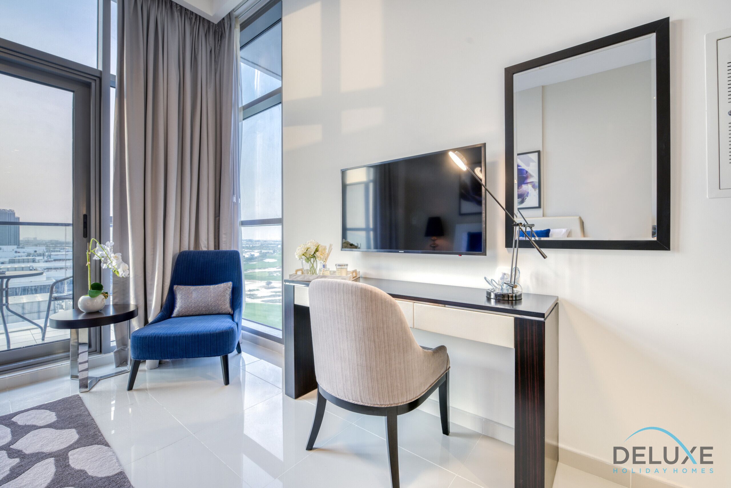 Une chambre moderne dotée d’une grande fenêtre, d’un bureau, de deux chaises, d’un miroir et offrant une vue sur la ville.