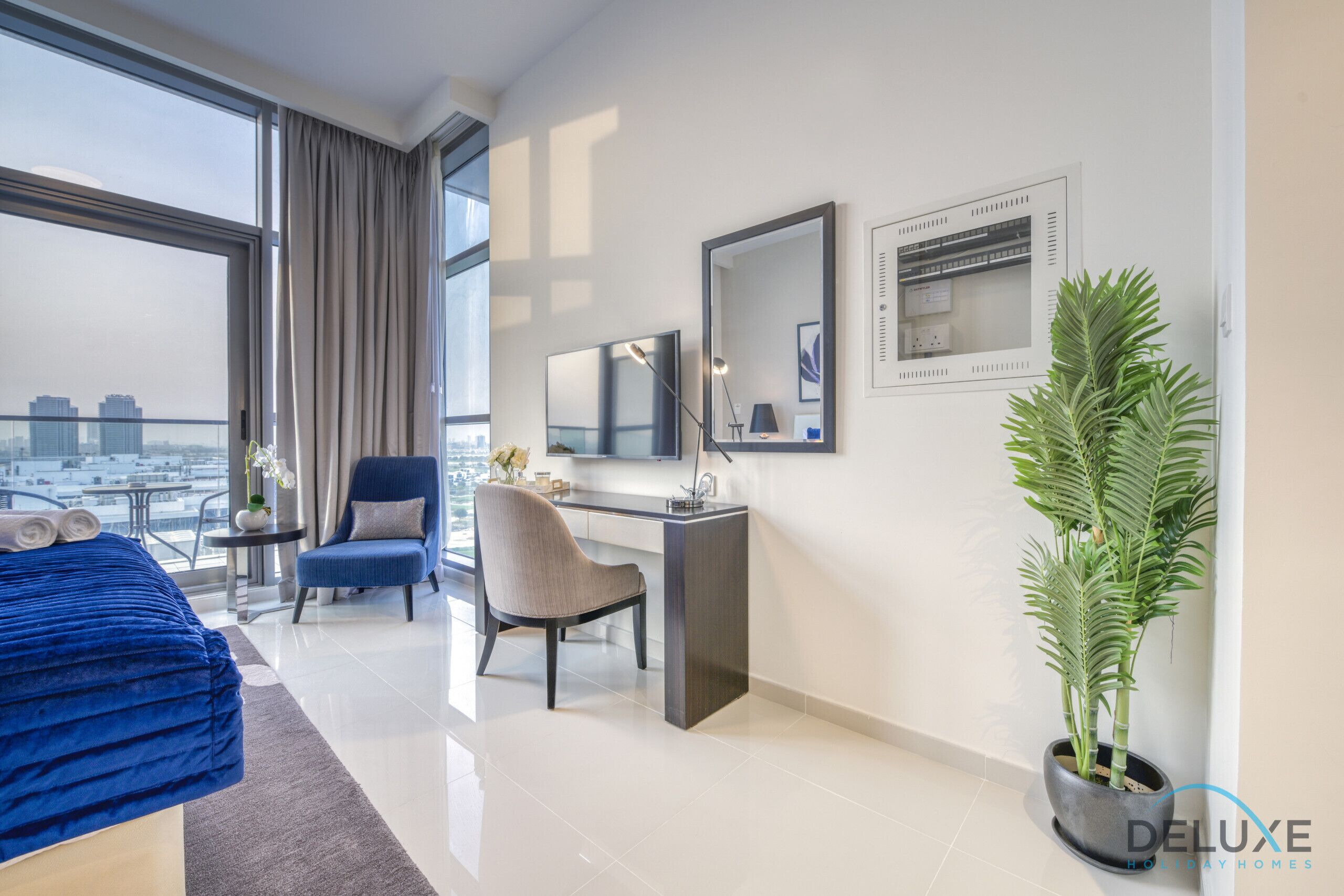 A modern hotel room with a large window, a bed, a desk, a chair, and a potted plant.