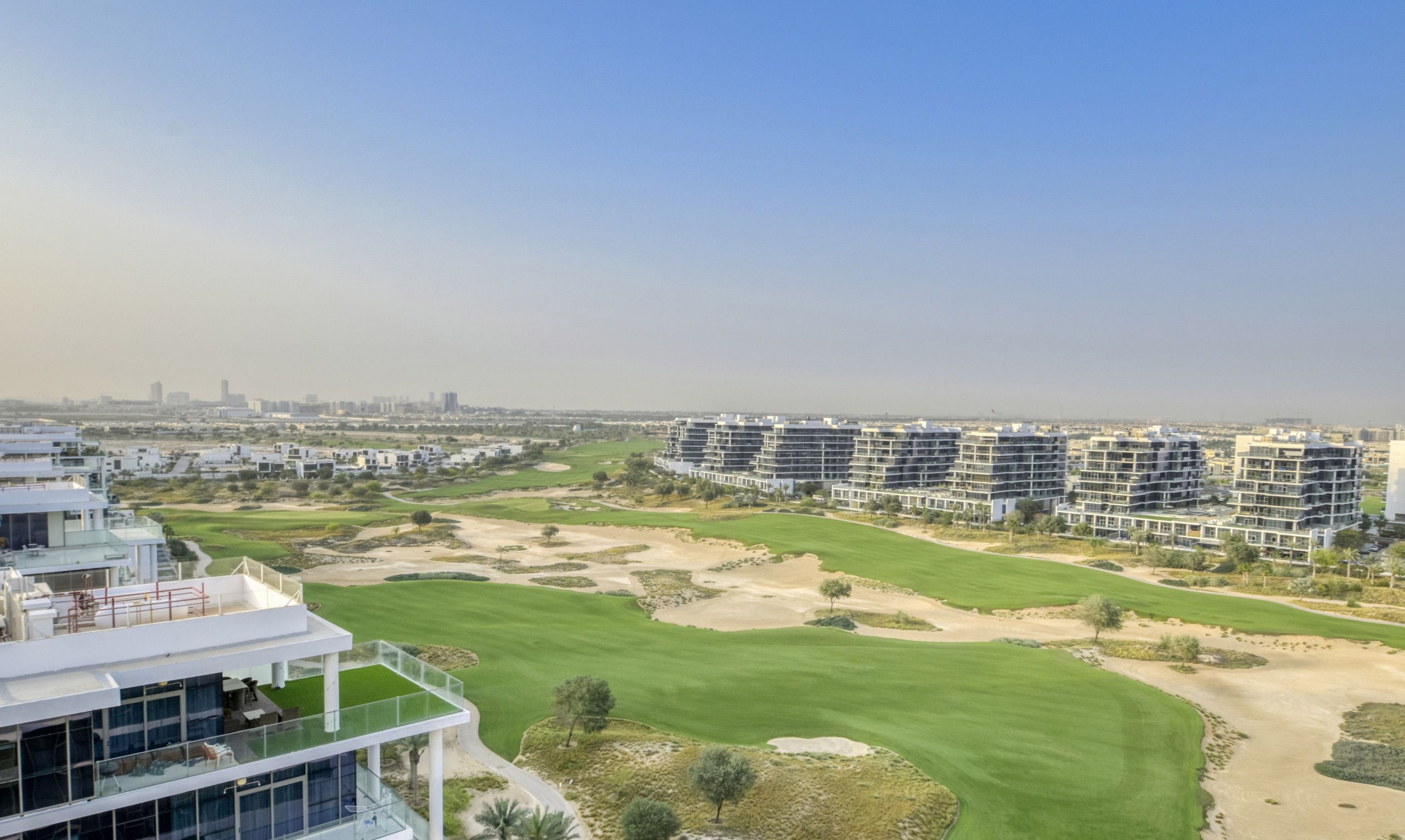 Un hotel moderno con varios pisos, un campo de golf y un horizonte urbano al fondo.