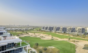 Un hotel moderno con varios pisos, un campo de golf y un horizonte urbano al fondo.